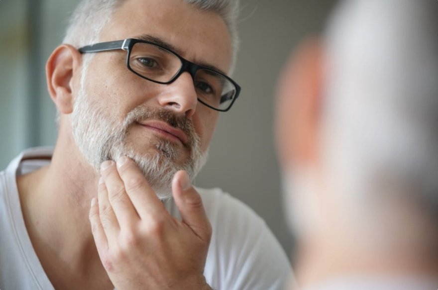 Man caring for his skin in a mirror while treating an ingrown hair on the beard area